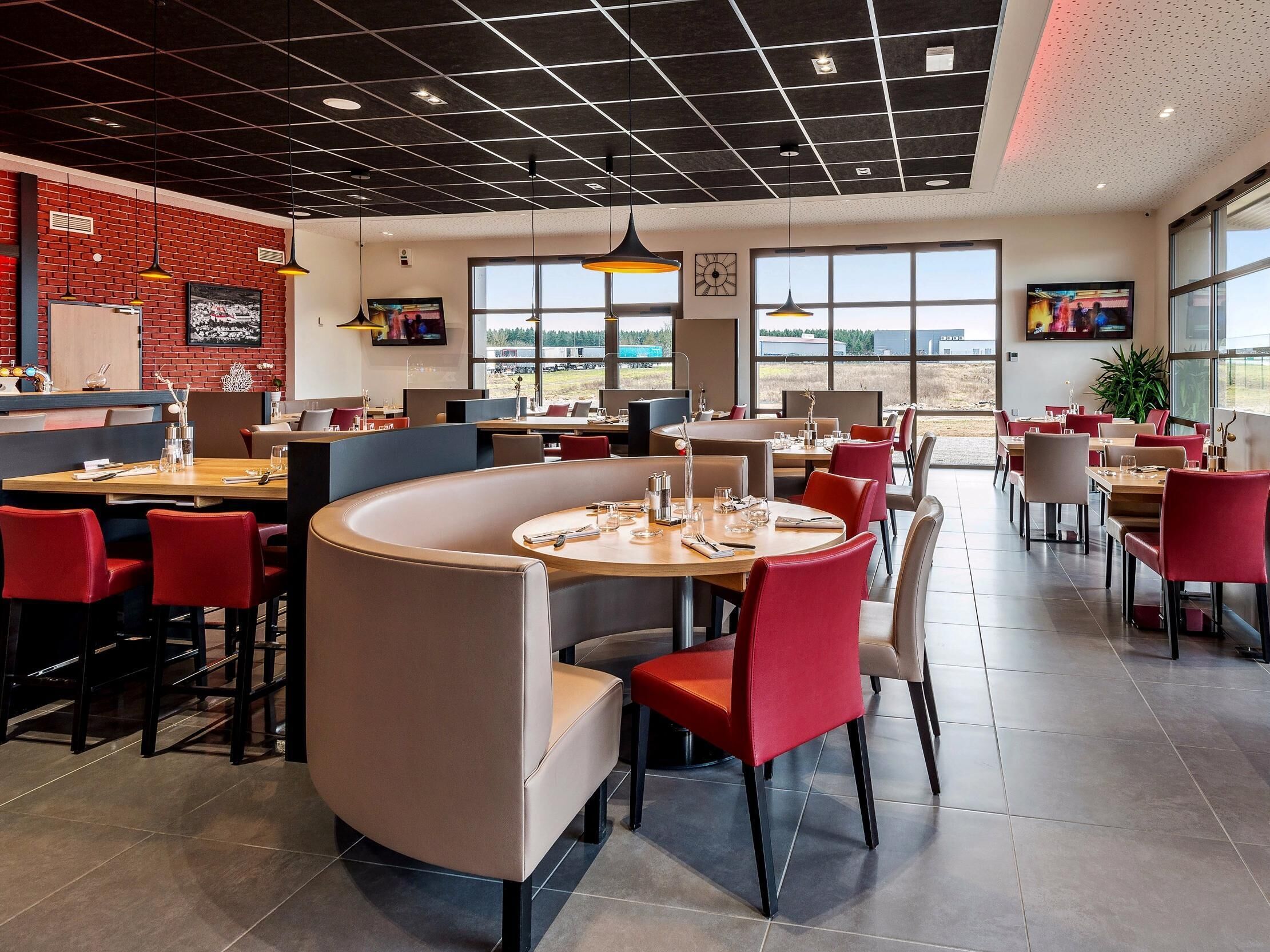 A modern restaurant with a brick wall, large windows, and red chairs.