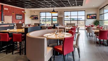 Ein modernes Restaurant mit Backsteinwand, großen Fenstern und roten Stühlen.