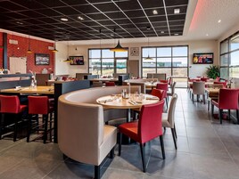 Un restaurante moderno con pared de ladrillo, amplias ventanas y sillas rojas.