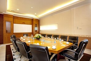 Une salle de conférence avec une longue table, des fauteuils en cuir noir, un tableau blanc et un arrangement floral au centre.