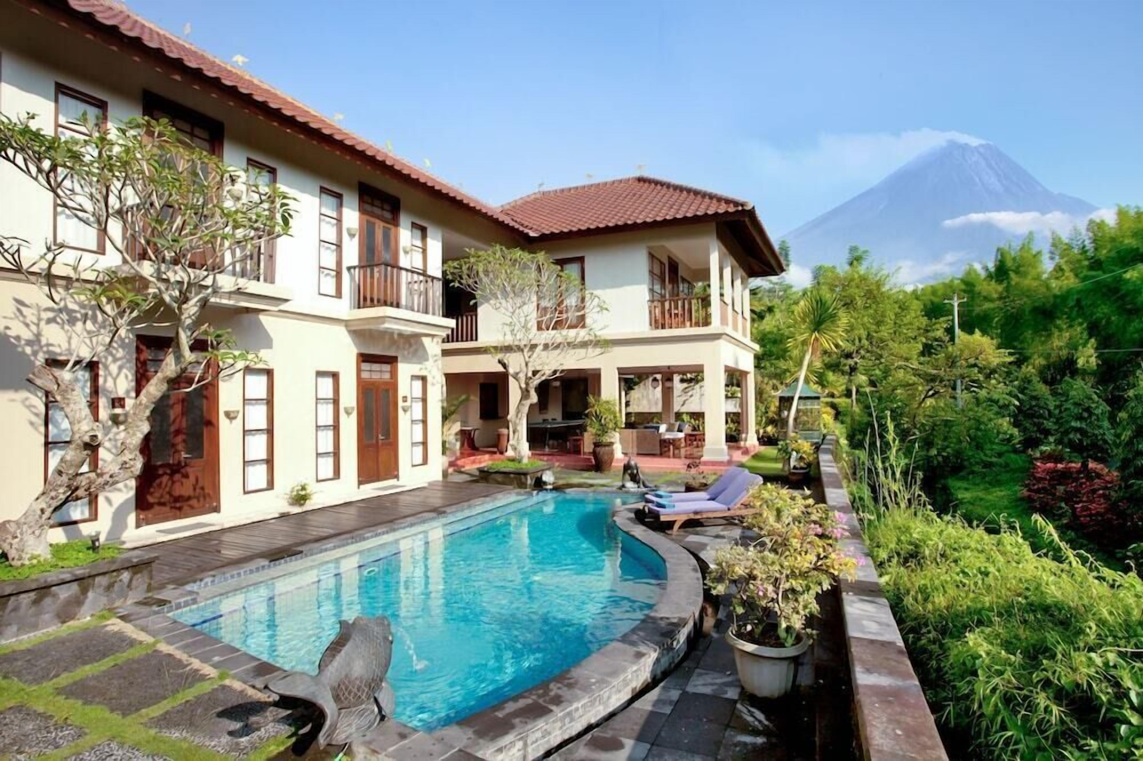 Un bâtiment à deux étages doté d’une piscine, entouré d’une végétation luxuriante et avec une montagne en toile de fond.
