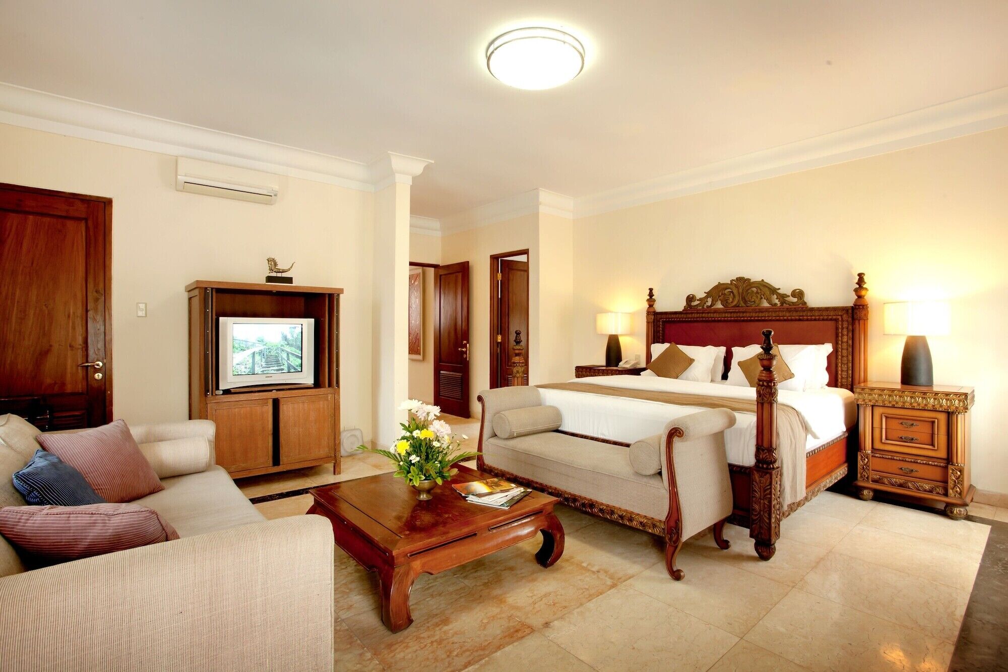 A hotel room with a bed, a sofa, a TV, a coffee table, and a lamp.