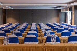 Une salle de conférence avec des rangées de tables, chacune recouverte d’une nappe bleue et blanche, et agrémentée de bouteilles d’eau et d’un pied de microphone.