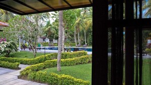 A view of a well-maintained garden with a pool, palm trees, and neatly trimmed hedges. - Umadewi Surf and Suites (Pekutatan)