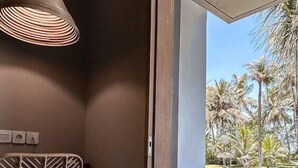 A room with a wooden door leading to a balcony with a view of palm trees. - Umadewi Surf and Suites (Pekutatan)