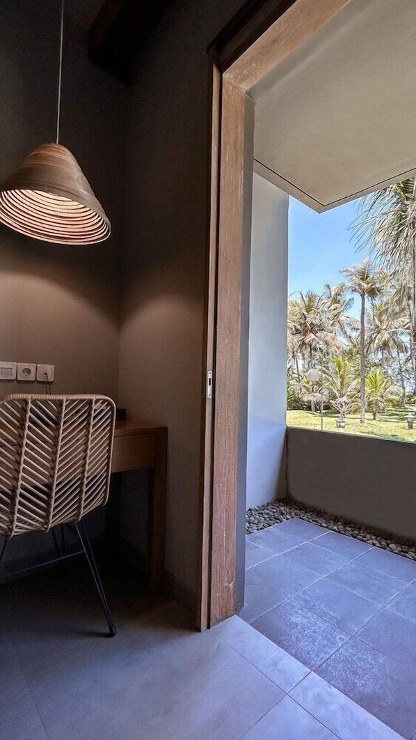 A room with a wooden door leading to a balcony with a view of palm trees. - Umadewi Surf and Suites (Pekutatan)