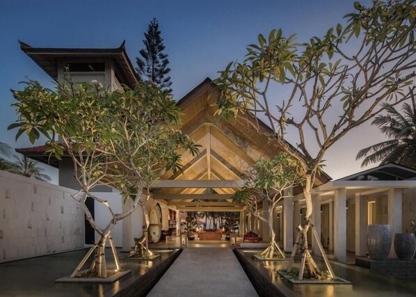 A modern building with a central atrium, surrounded by trees and a pathway leading to the entrance. - Umadewi Surf and Suites (Pekutatan)