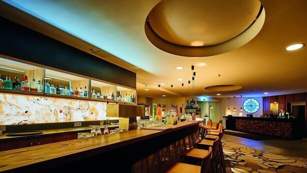 A bar area with a long counter, multiple stools, and a variety of bottles and glasses on shelves. - 4moods Suites and Spa Erwachsenenhotel (Bad Griesbach im Rottal)