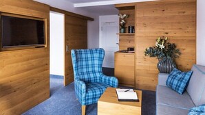 A room with a blue plaid armchair, a grey sofa, a wooden coffee table, and a TV mounted on a wooden wall. - 4moods Suites and Spa Erwachsenenhotel (Bad Griesbach im Rottal)