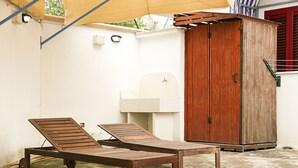 Une terrasse avec deux fauteuils de jardin en bois, un meuble en bois et un évier blanc.