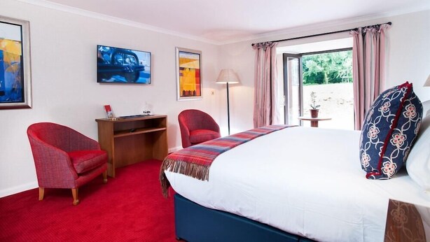 A hotel room with a bed, a desk, two chairs, a TV, and a window with curtains. - Parkway Hotel and Spa (Cwmbran)