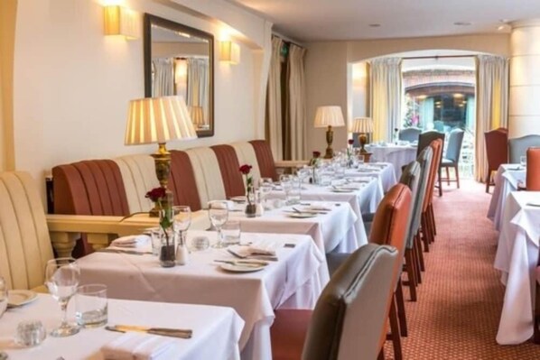 A formal dining room with tables set for service, a sofa with cushions, and a mirror on the wall. - Parkway Hotel and Spa (Cwmbran)