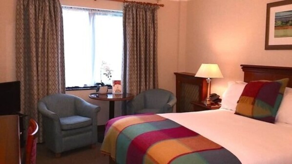 A hotel room with a bed, two armchairs, a small table, a lamp, and a window with curtains. - Parkway Hotel and Spa (Cwmbran)