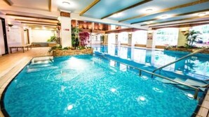 An indoor swimming pool with clear water, surrounded by a tiled floor and a wooden deck. - Parkway Hotel and Spa (Cwmbran)