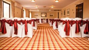 A hotel room with a checkered floor, white chairs with red sashes, and a hallway leading to a door. - Parkway Hotel and Spa (Cwmbran)