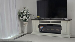 A modern living room with a grey sofa, a flat-screen TV on a white entertainment unit, a chandelier, and a vase of flowers. - Charming 3-bedroom Guest house in enchanting San Jose with AC (San Jose)