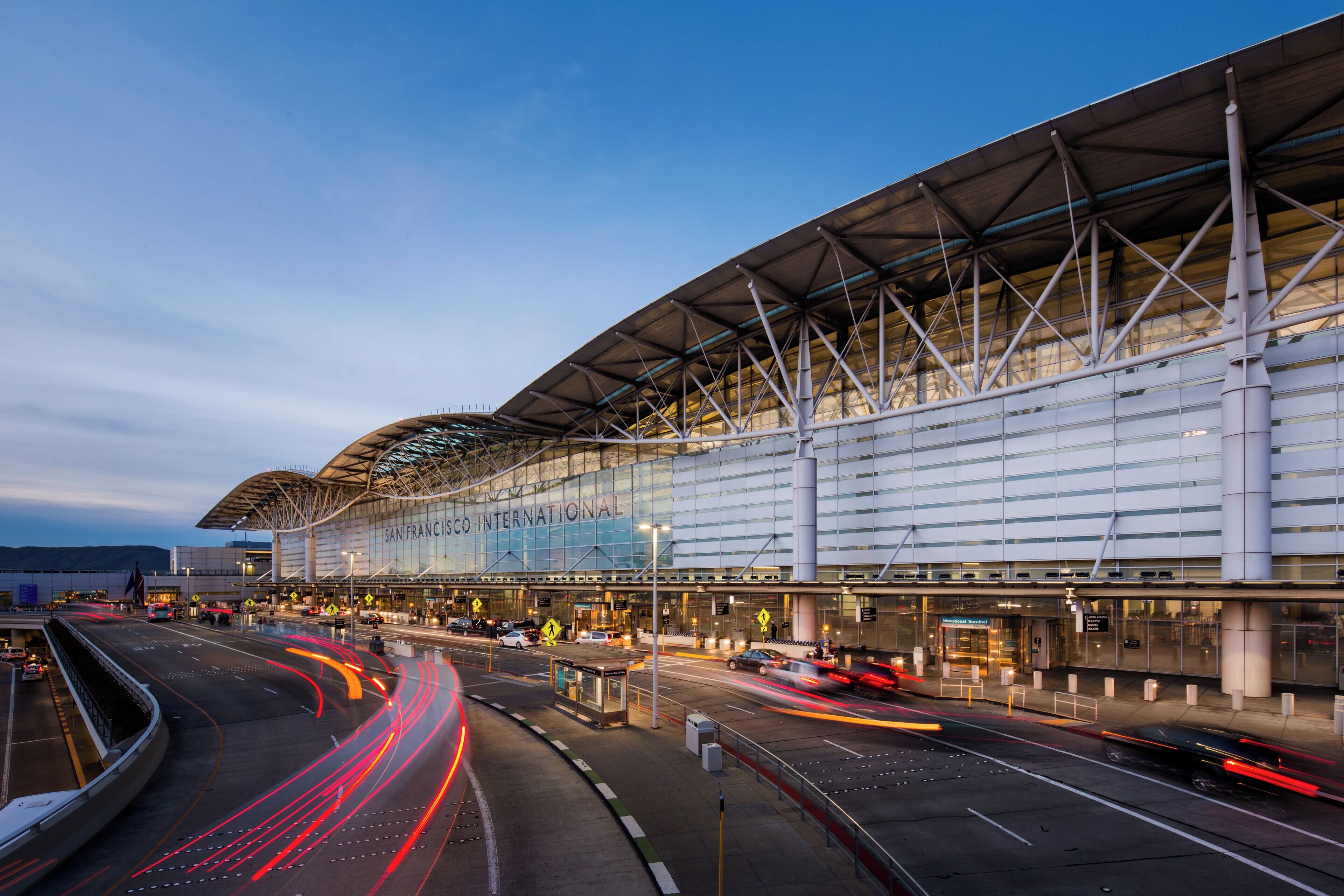 Una moderna terminal de aeropuerto con una amplia fachada de vidrio, múltiples accesos y una estructura de techo curva.