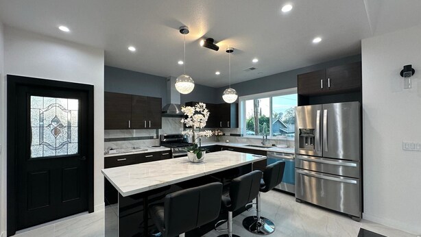 A modern kitchen with dark cabinets, a large island with bar stools, stainless steel appliances, and a decorative chandelier. - Charming 3-bedroom Guest house in enchanting San Jose with AC (San Jose)