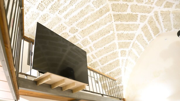 A staircase with a wooden handrail and a black object on the landing. - Two-story La Volta Court (Tuglie)