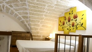 A bedroom with a brick ceiling, a wooden bed, a nightstand with a lamp, and a wall with floral paintings. - Two-story La Volta Court (Tuglie)