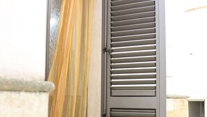 A door with a yellow curtain and a metal shutter. - Two-story La Volta Court (Tuglie)