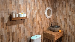 Ein Badezimmer mit einem Holzbadezimmer-Möbel, einem runden Spiegel und Pflegeprodukten auf einem Regal.