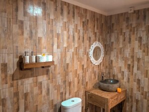 Une salle de bain avec un meuble-lavabo en bois, un miroir rond et des articles de toilette rangés sur une étagère.