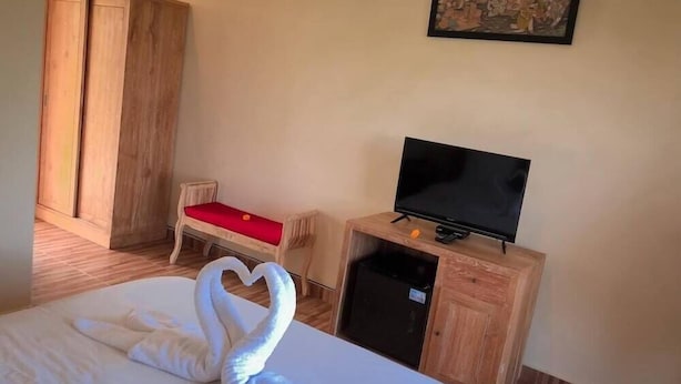 Ein Hotelzimmer mit Bett, Fernseher auf einem Holzboden, Kleiderschrank und einem roten Sessel.