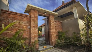 Ein modernes Haus mit Backsteinfassade, Betonauffahrt und kleinem Garten mit tropischen Pflanzen.