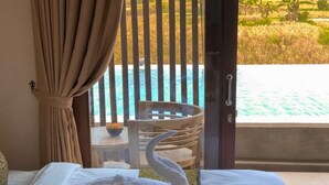 Ein Hotelzimmer mit Bett, einem schwanenförmigen Handtuch, einem Tisch mit Schüssel und Blick auf einen Swimmingpool.