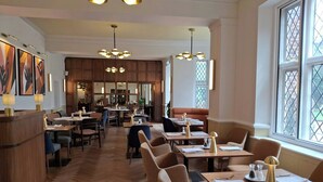 Interior de un restaurante con suelo de madera, varias mesas, sillas e iluminación colgante.