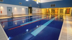 Una piscina interior con carriles delimitados, suelo de baldosas azules y pared azul y blanca.