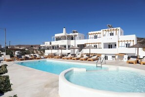 A pool area with lounge chairs and umbrellas, surrounded by white buildings with a modern architectural style. - Irida Luxury Apartments (Naxos)