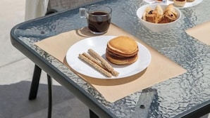 A glass table with a plate of churros, a cup of coffee, and a plate of pastries. - Irida Luxury Apartments (Naxos)
