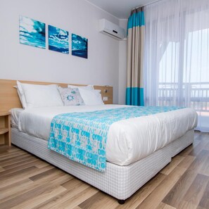 A neatly made bed with a patterned blanket, a wooden headboard, and a wall-mounted air conditioner. - Nevis Resort & Aqua Park - All Inclusive (Nessebar)