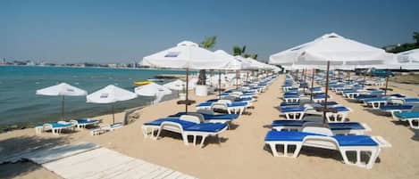 A beach with rows of sun loungers and umbrellas, a wooden walkway, and a clear view of the sea.