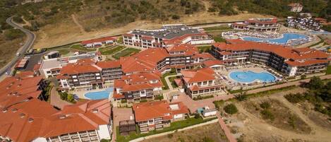 An aerial view of a resort with multiple buildings, a large swimming pool, and a winding road.