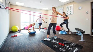 A gym with exercise equipment, a black mat with 'KNEE' branding, and a window with a view. - Hotel 47 (Konstanz)
