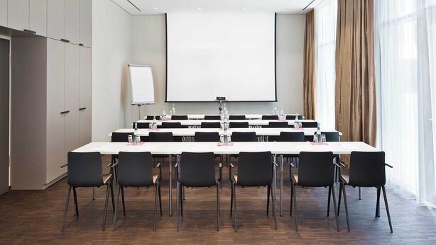 A conference room with a large table, chairs, a projector screen, and a whiteboard. - Hotel 47 (Konstanz)