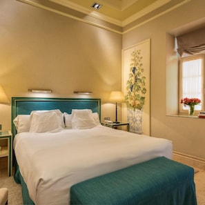 A hotel room with a bed, a nightstand, a lamp, a vase with flowers, and a painting on the wall. - Hotel Casa del Poeta (Seville)