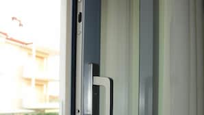 A sliding glass door with a metallic handle, leading to an outdoor balcony with a white chair and a small table. - Sunway Hotel (Kassandra)