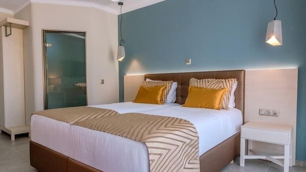A modern hotel room with a large bed, a bedside table, and a glass door leading to a bathroom. - Sunway Hotel (Kassandra)