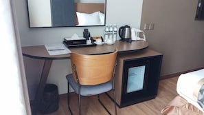 A compact hotel room with a small desk, a chair, a bed, a mirror, a coffee maker, a kettle, and a trash bin. - Roxy Hotel Apartment (Kuching)
