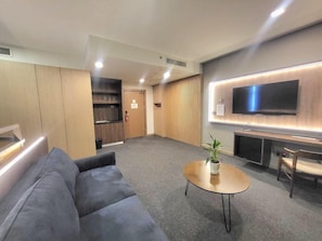 A modern living room with a grey sofa, a round coffee table with a plant, a flat-screen TV mounted on the wall, and a wooden cabinet. - Roxy Hotel Apartment (Kuching)