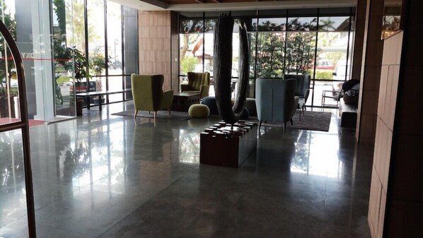 Eine geräumige Lobby mit poliertem Boden, einer Sitzecke mit Stühlen und einer Couch, und großen Fenstern mit Blick ins Freie.