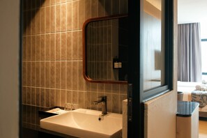 A bathroom with a white sink, a mirror, and a window. - Roxy Hotel Apartment (Kuching)