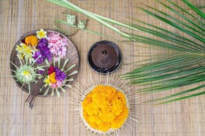 A bamboo mat with a wooden plate containing flowers and a bowl of yellow powder. - Tapa Nata Ubud by Pramana (Ubud)
