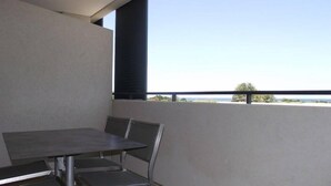 Un balcon avec une table et des chaises, une vue sur la mer et un ciel dégagé.