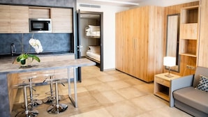 Une cuisine moderne dotée d’un four à micro-ondes encastré, un coin repas avec des tabourets de bar, une armoire en bois et une petite table de chevet avec une lampe.