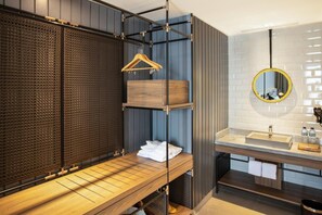 A modern bathroom with a wooden bench, a hanging wooden hanger, and a round mirror with a yellow frame. - Porta by The Ambarrukmo (Depok)